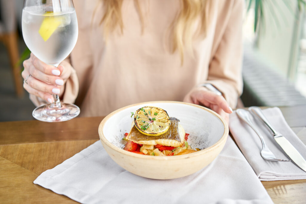 Roasted Halibut with vegetables, paprika pepper and pumpkin cream. Lunch in a restaurant, a woman eats delicious and healthy food. Dish decorated with a slice of lemon. Restaurant menu.